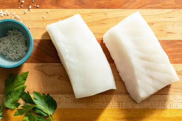 Fresh cod fillets on a wooden cutting board with sea salt and parsley