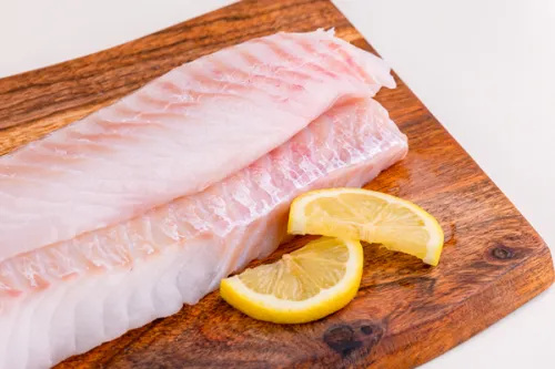 Fresh cod fillets with lemon slices on a wooden board