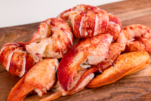 Fresh lobster meat, including tail and claw pieces, arranged on a wooden board